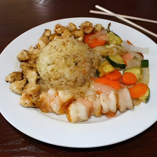 Hibachi chicken, shrimp, fried rice, and mixed vegetables on a white plate with chopsticks.