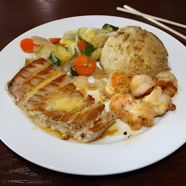 Hibachi meal with grilled fish, shrimp, scallops, fried rice, and mixed vegetables on a white plate.