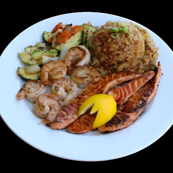 Hibachi salmon and shrimp with fried rice, grilled vegetables, and a lemon wedge on a white plate.