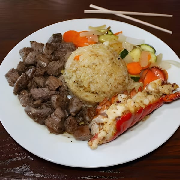 Hibachi steak, lobster, fried rice, and mixed vegetables on a white plate with chopsticks.