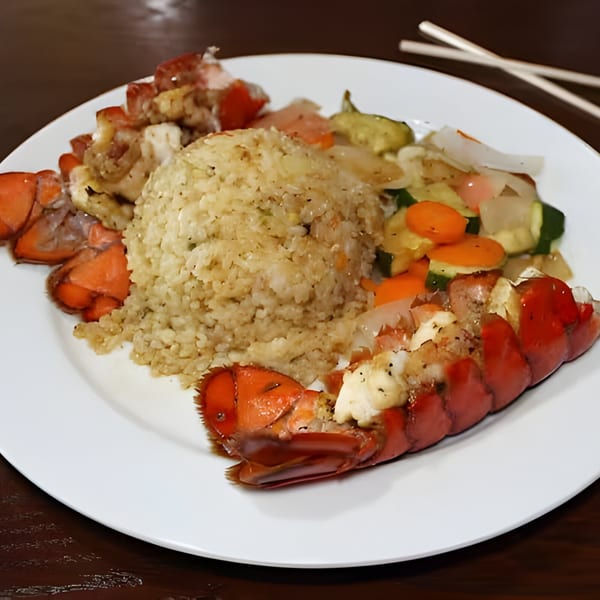 Hibachi lobster tails, fried rice, and mixed vegetables on a white plate with chopsticks.